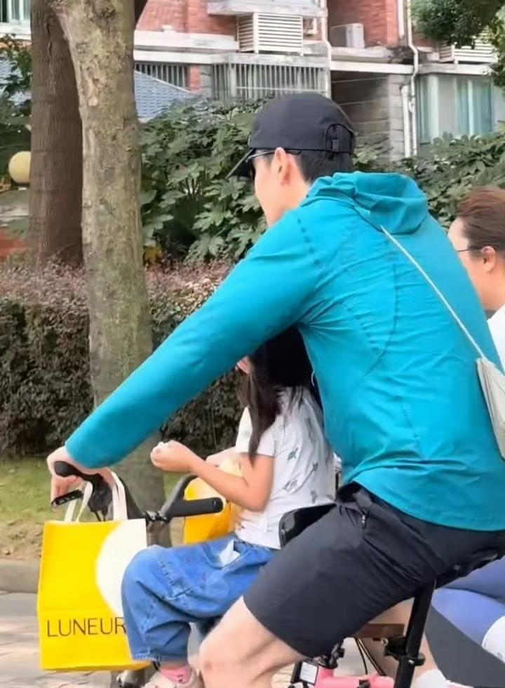 胡歌一家三口骑行被偶遇，胡歌带着女儿，把她放在前面儿童椅上坐，还用手臂挡住女儿的
