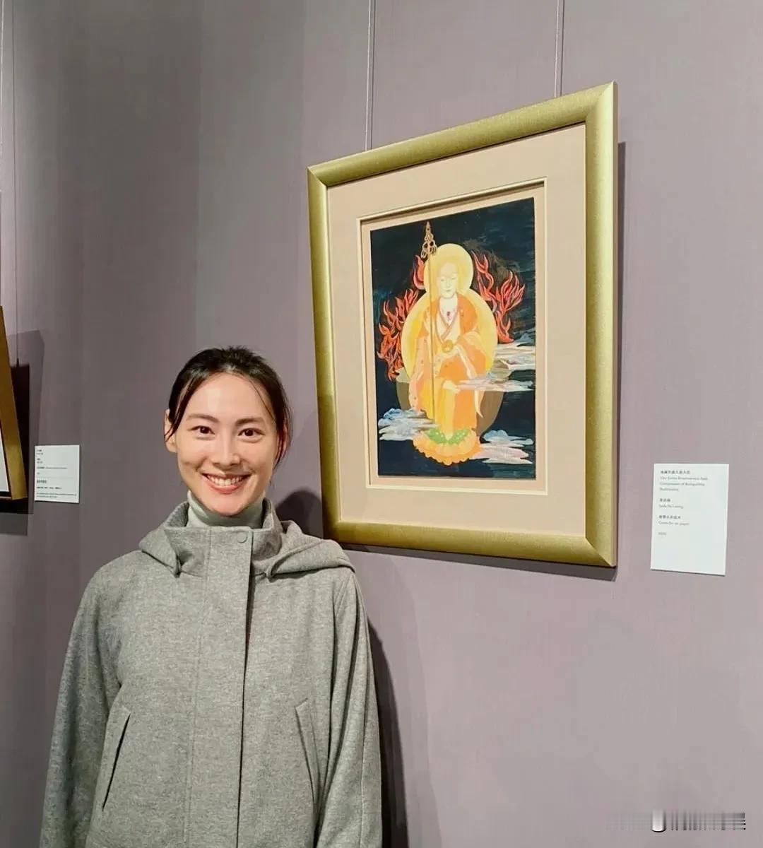 梁洛施在画展和自己的画作同框，她的作品是一幅《地藏王菩萨》图。
她素颜出现在画展
