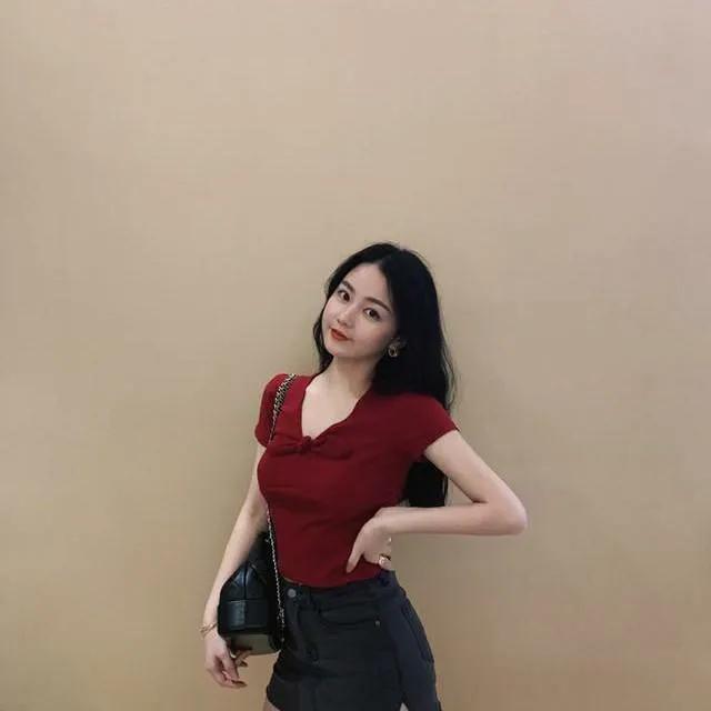 红衣美人倚墙立，轻抚腰间意自闲。