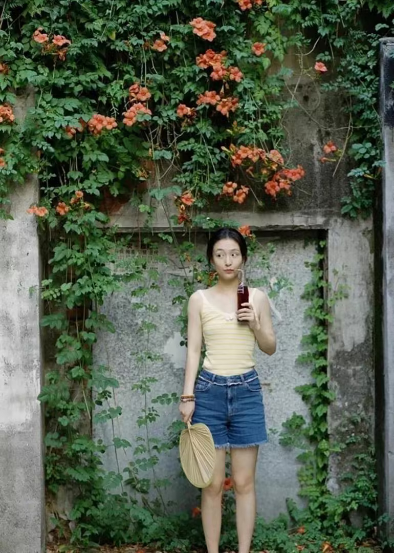 吴倩身穿黄白条纹吊带配高腰蓝牛仔短裤，光脚蹲在老巷的小马扎上啃西瓜，这一身很夏日
