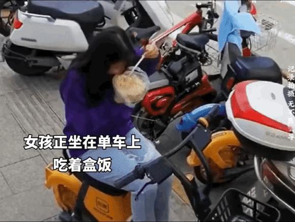 监控记录下的感人一幕。路边，一女孩正坐在电动车上专心地吃着盒饭，这时，一流浪汉突