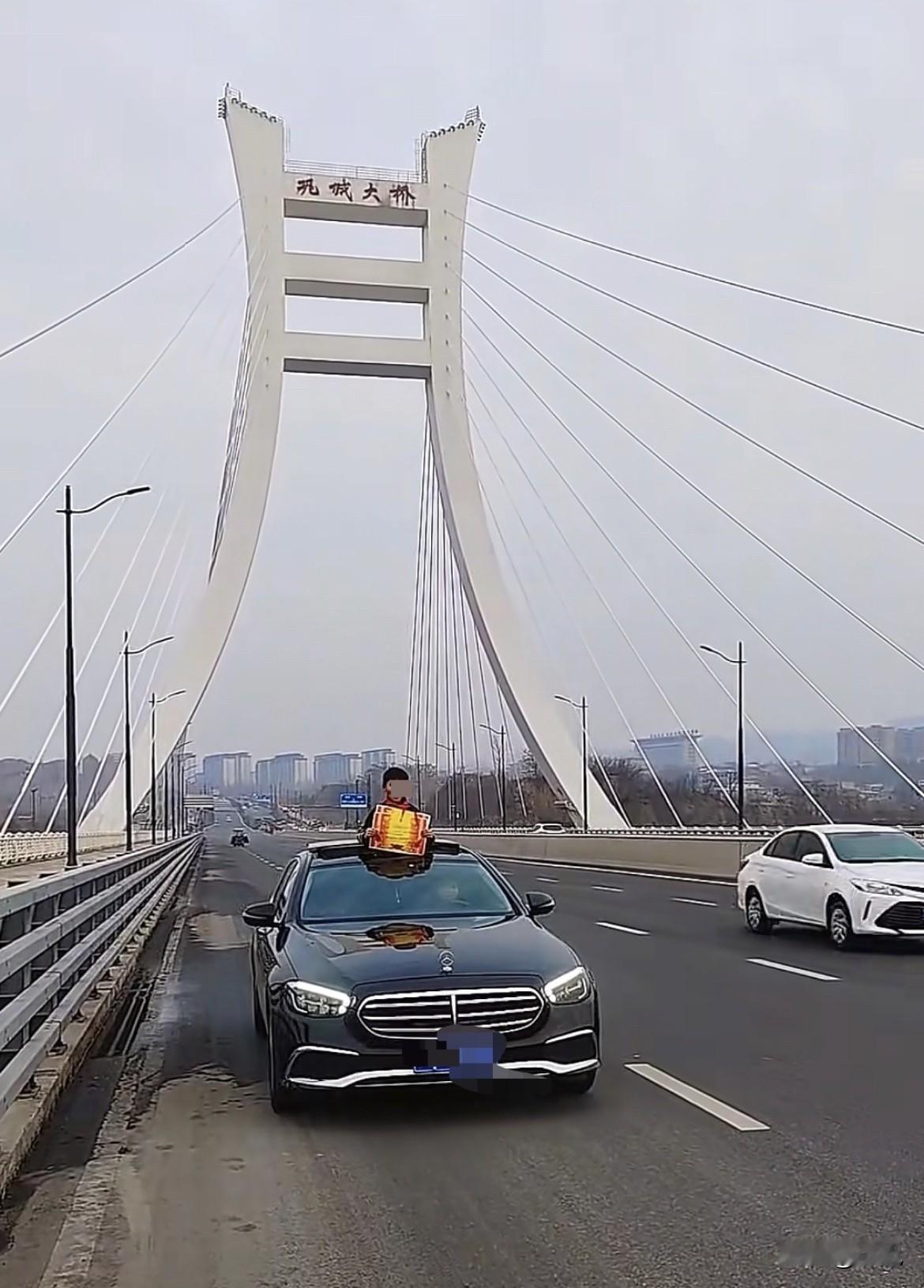 孩子站天窗上秀奖状，结果奖状是网上买来的。
河南巩义大桥上，一辆黑色轿车开着天窗