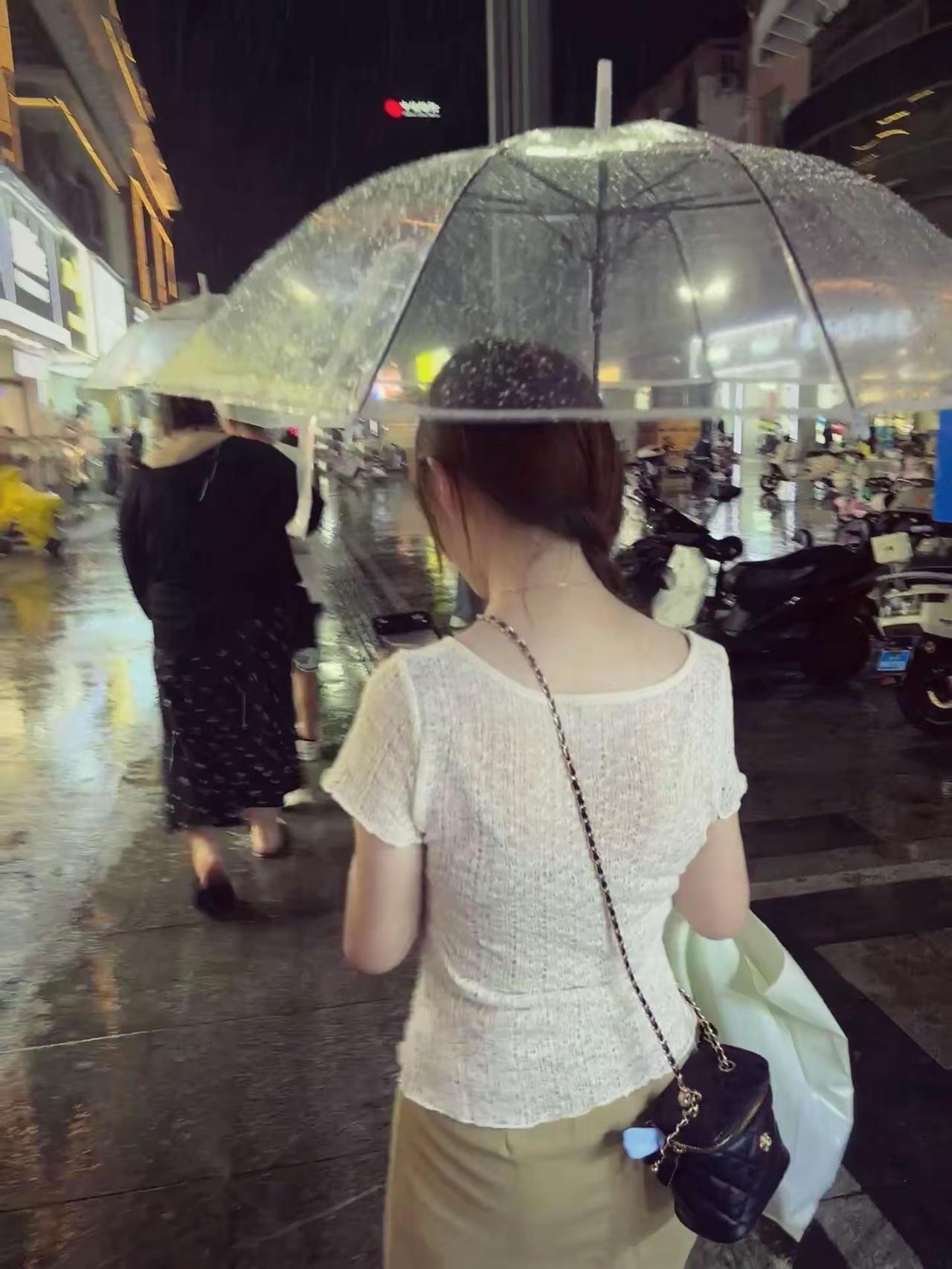 雨夜长街，伞落微雨，灯火映湿路面。
一身简约素色，独自穿行在都市夜色里，朦胧光影