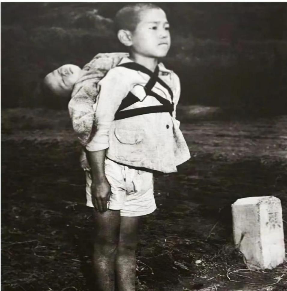 1945年，一名10岁的日本男孩抿着嘴，笔直地背着弟弟。而弟弟头向后仰，早已气绝