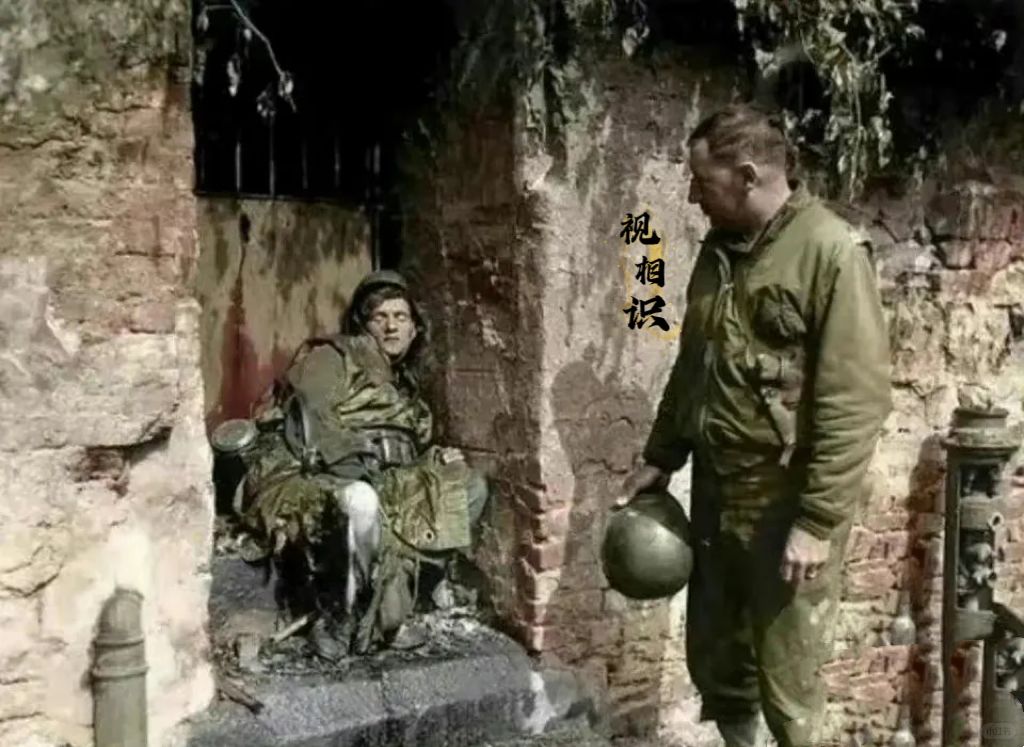 1945年，一美军士兵看着一位已经死去的纳粹士兵，他的头靠在墙边，面容安详，从他...