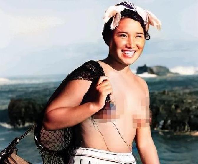 1955年，一名身体强壮的日本女人赤裸上半身，背着一个黑色的编织袋站在海边。这个