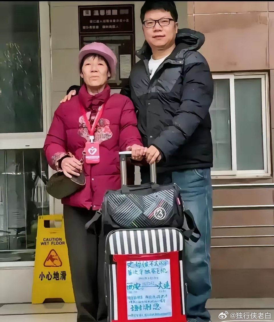 机场里，小伙子给丈母娘送行，老人的行李箱上贴着一张纯手工写的大海报，上面写着:“