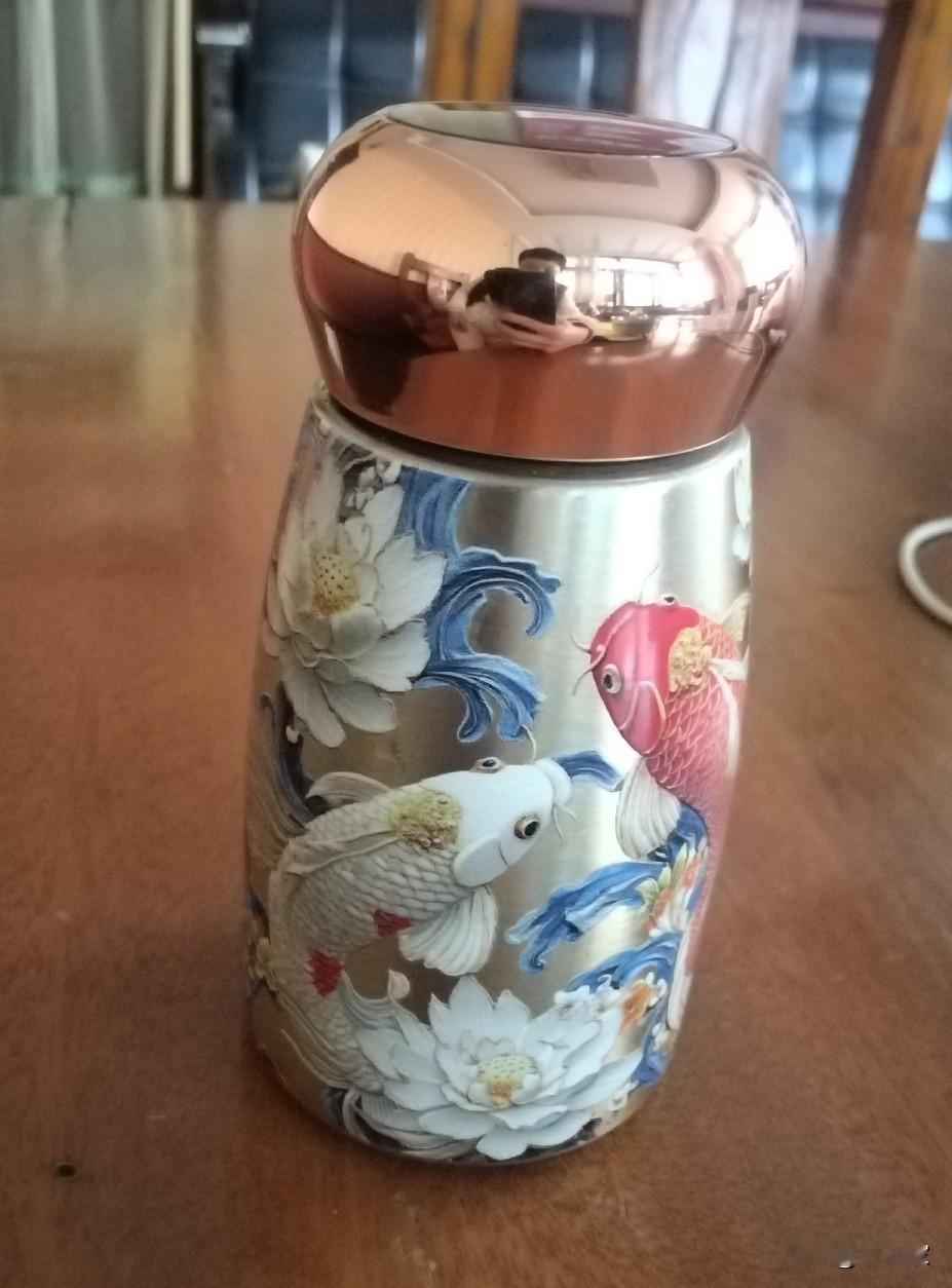 这只水杯往桌上一放，连木纹都沾了几分灵气。

银亮杯身裹着立体的锦鲤与白莲，红鲤