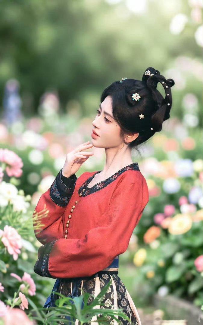 鞠婧祎新剧唐装造型路透繁花簇拥红衣佳人，精巧发髻缀着细碎珠钗。立于烂漫花丛间，抬