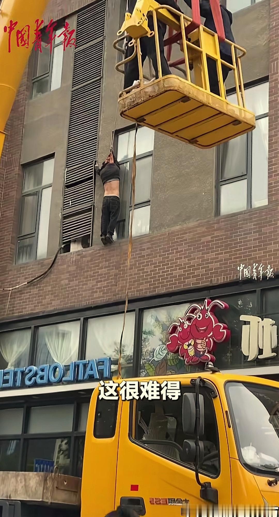 空调维修工人在拆装空调时从高处坠落，被绳索套住脖子和手悬在高空。
发生在北京的这