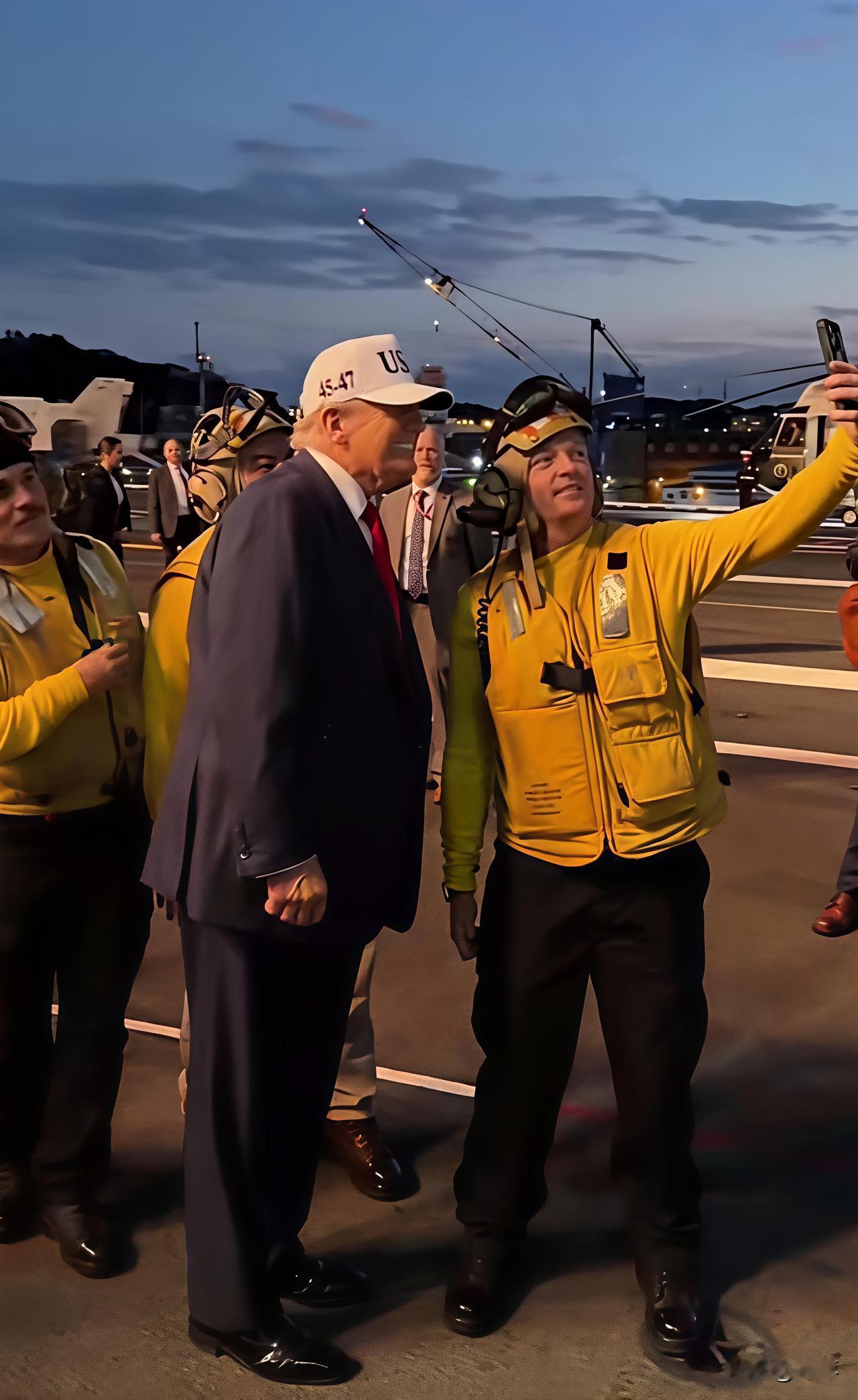 美国总统特朗普登上华盛顿号航空母舰当他走过时，穿黄马甲的工作人员拿出收手机向他示