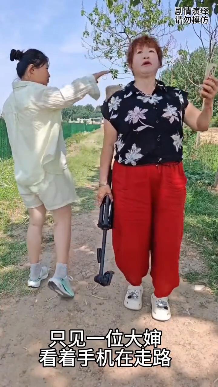女子整蛊大婶，把她的帽子摘掉。
女子正在走路时，只见一位大婶看着手机在走路，然后