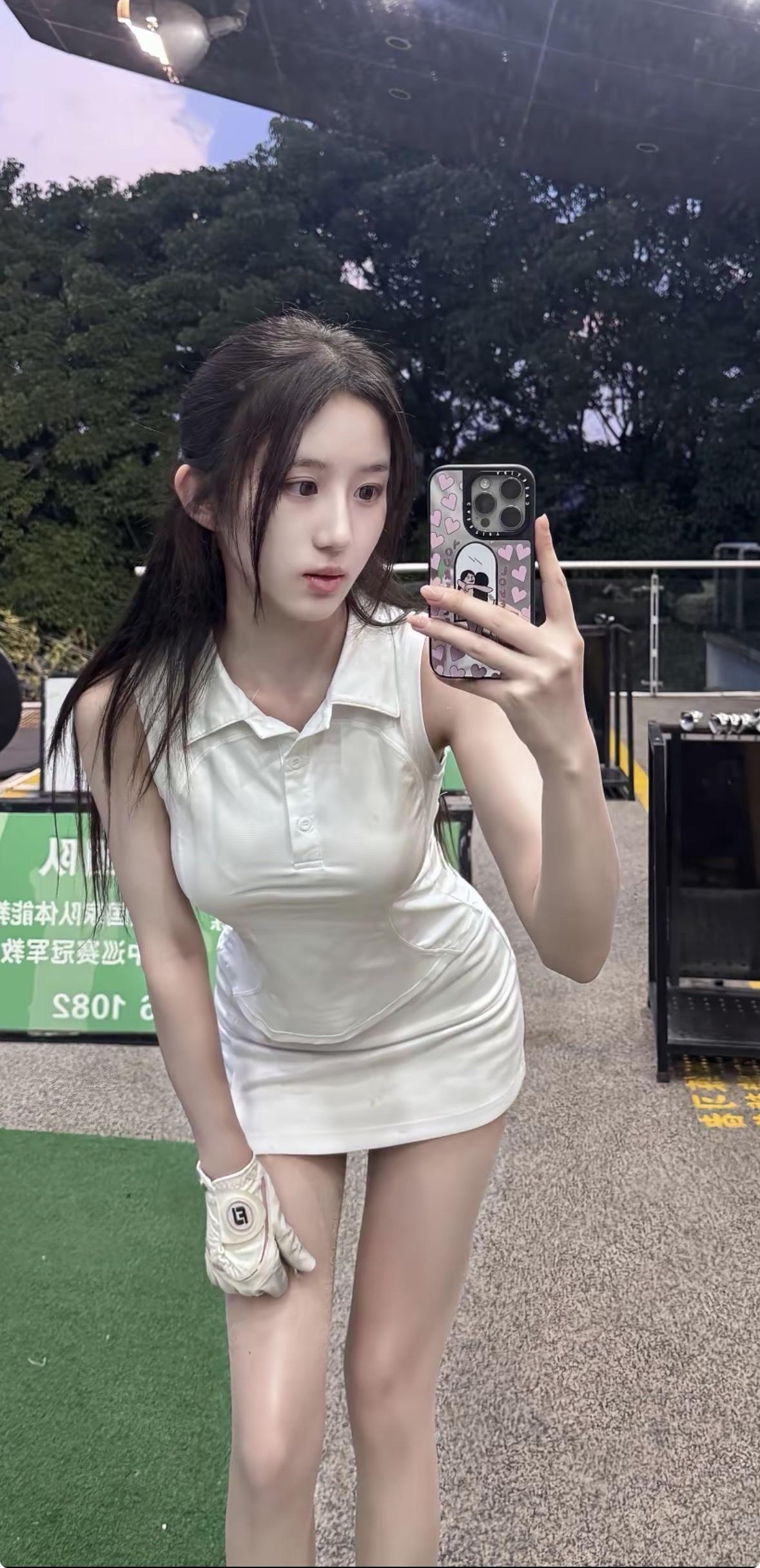 一位年轻女子坐在舒适的米色沙发上，低头专注地看着手中的手机。她身穿白色无袖Pol