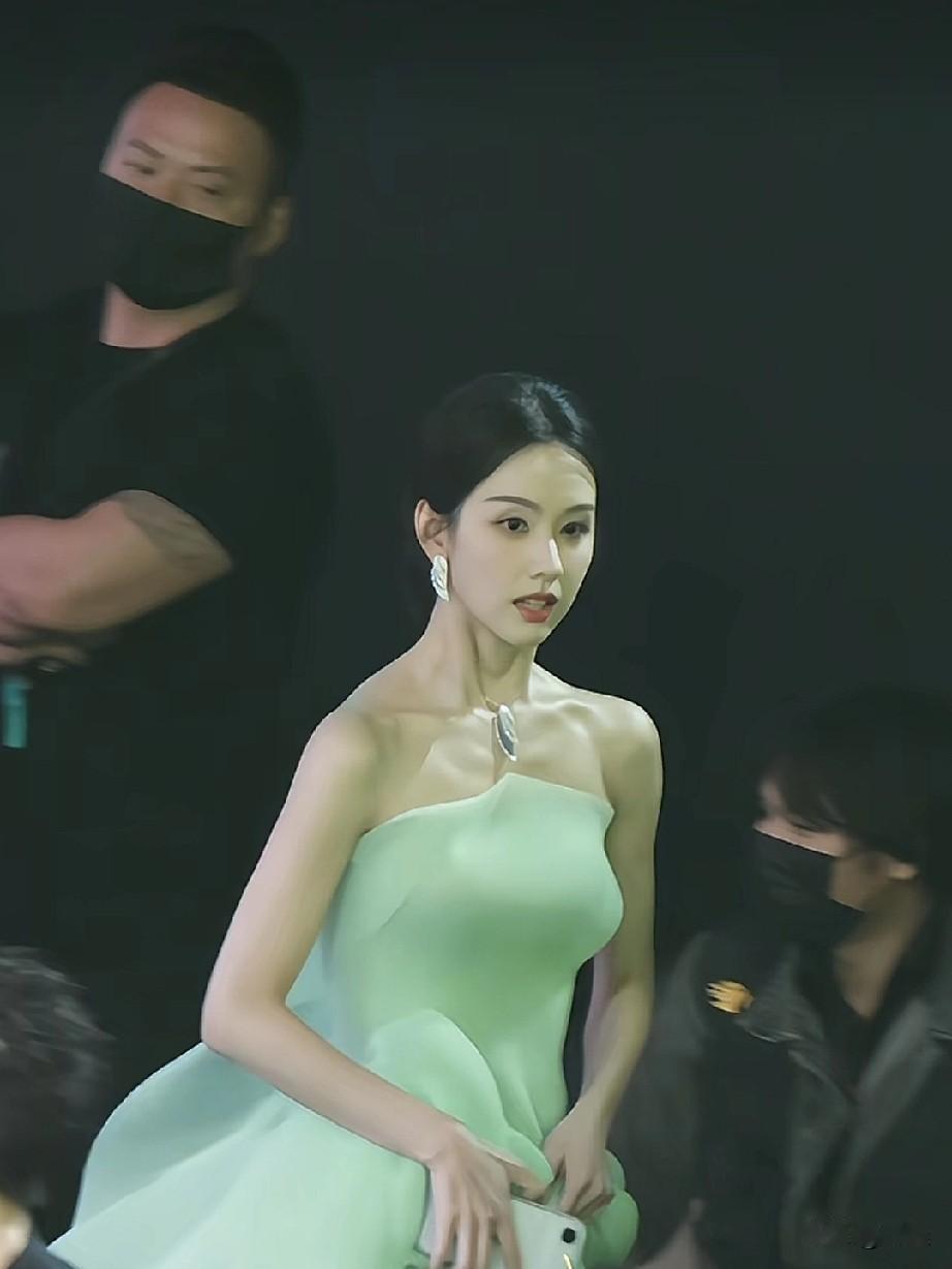 陈都灵身着一袭清新的浅绿色礼服，手持奖杯站在舞台的麦克风前，在参加某个颁奖典礼或