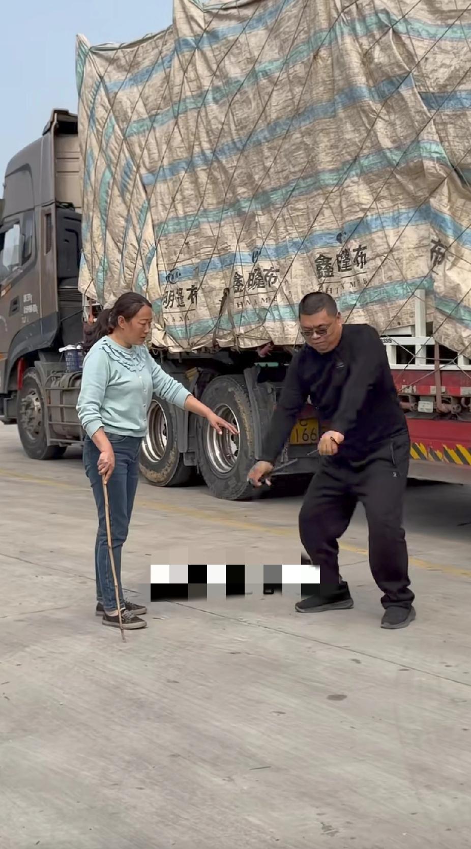 路边的一辆大货车旁，拿着臂力棒锻炼的男子身旁，竟然站着一名手拿木棍的女子，知道真