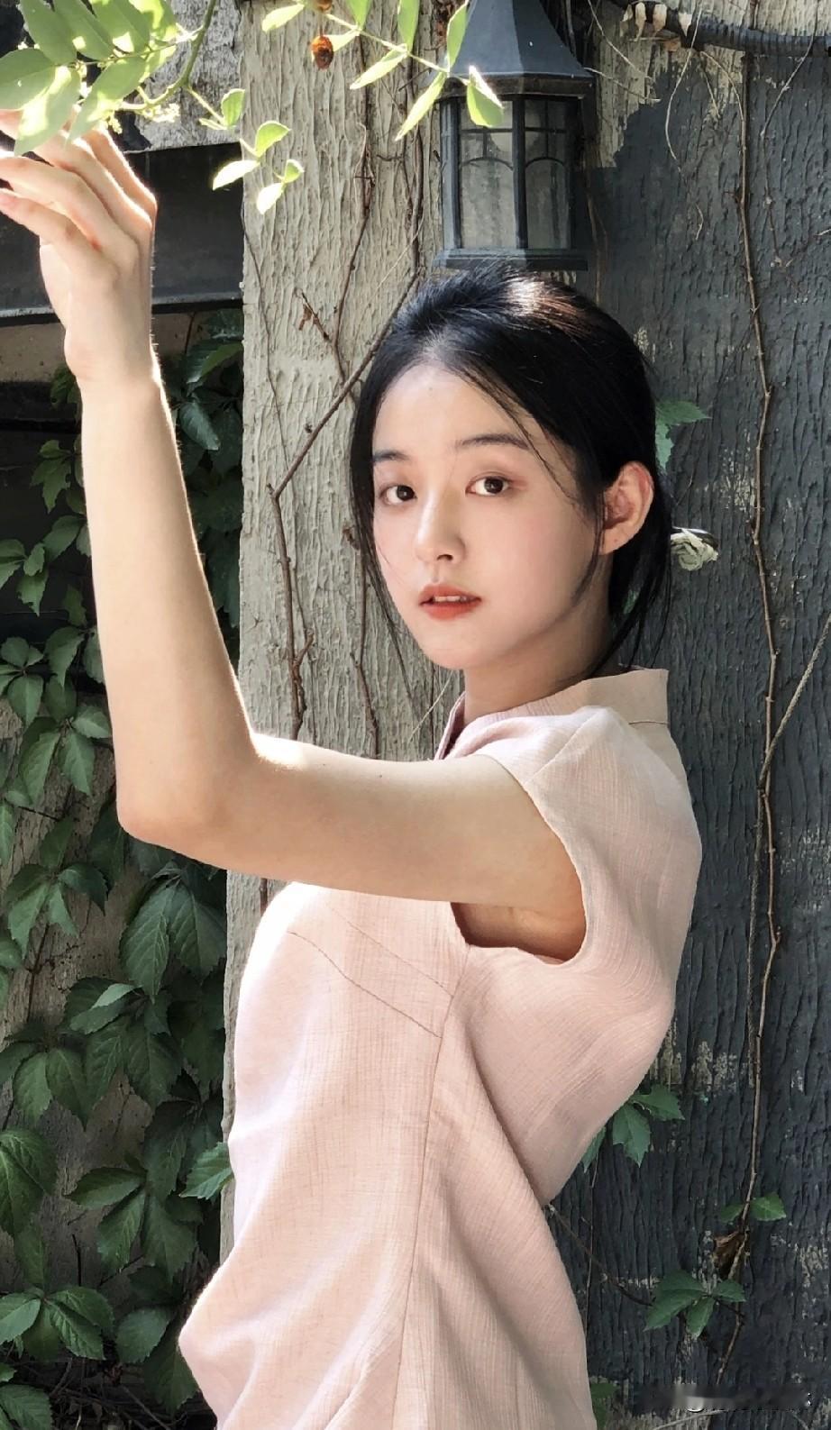 少女在树旁轻抚绿叶，阳光洒下温暖的光影