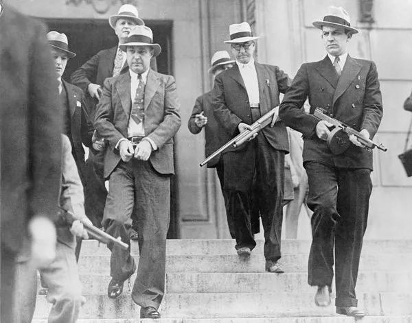 1933 年，乔治·凯利·巴恩斯被捕，他的绰号是“机关枪凯利”。他周围是手持汤普