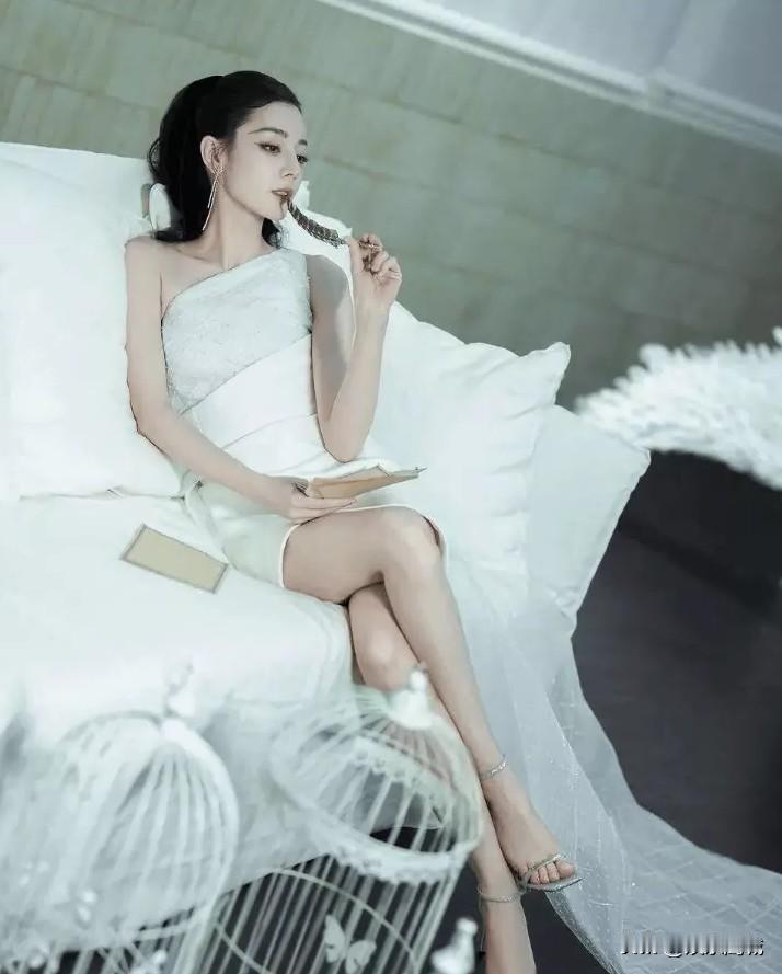 迪丽热巴一袭白裙斜肩设计，宛如仙子下凡。单肩巧露香肩，另一侧布料轻绕腰间，勾勒出