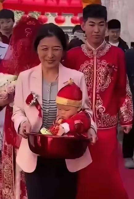 红棉袄刚穿上，

娃的唐装还没烫平，

她抱孩子站门口时手在抖。

这不是什么感