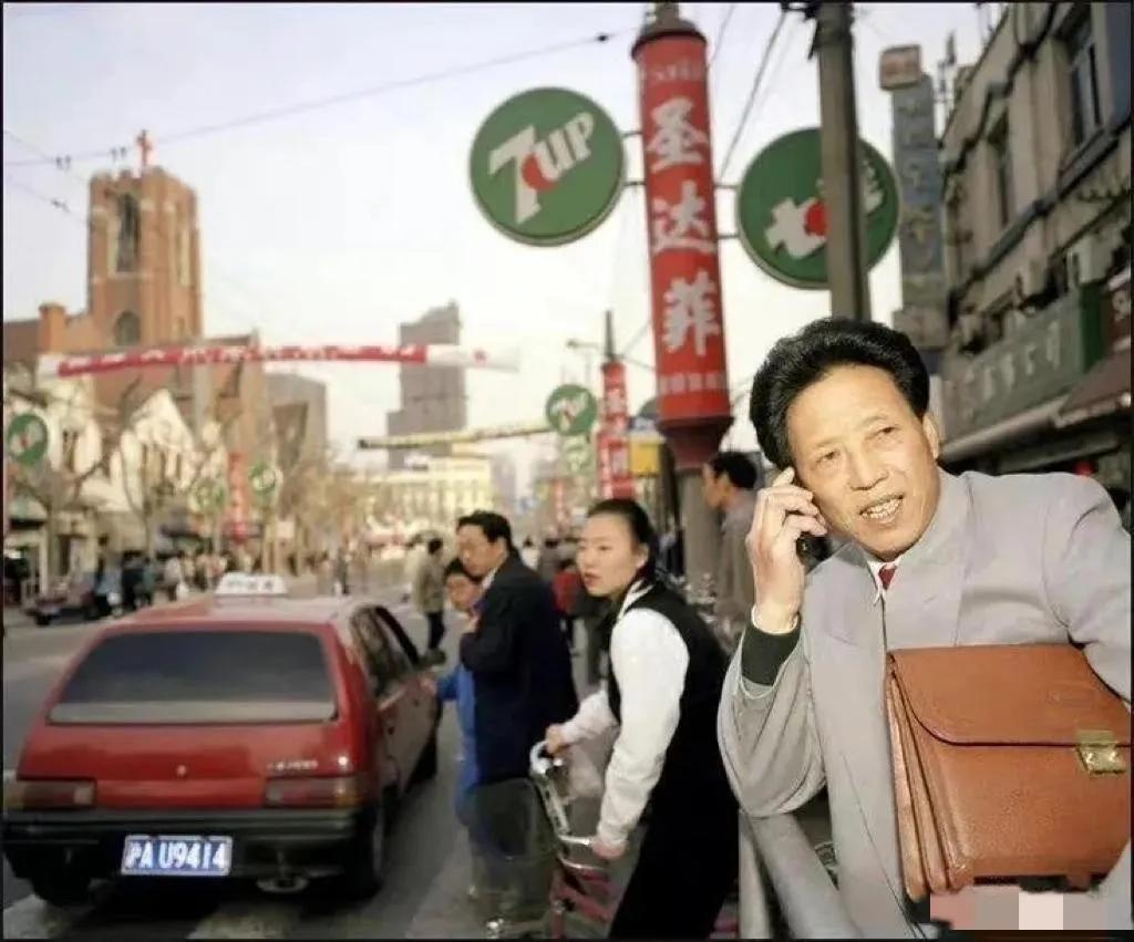90年代的上海，一个西装革履的暴发户，正在路边拿着手机打电话，引起了路人的瞩目。