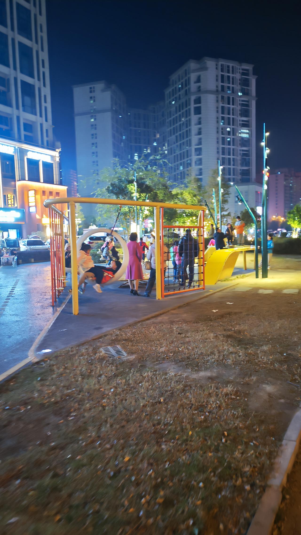 夜晚的公园里，孩子们在游乐场尽情玩耍，灯光映照出欢快的氛围。