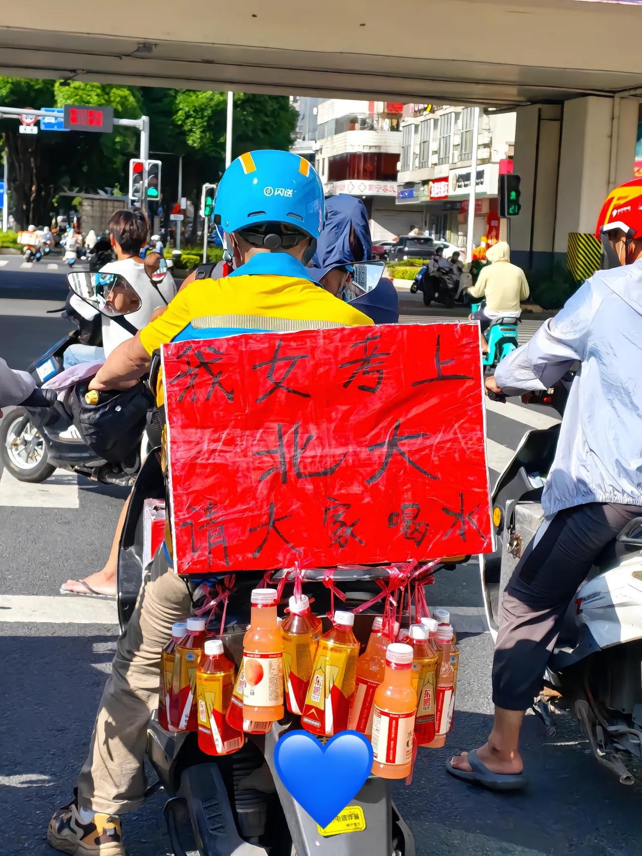 广西南宁，一辆外卖车的后座挂满饮料，红纸黑字写着“女儿考上北大，免费自取”。
