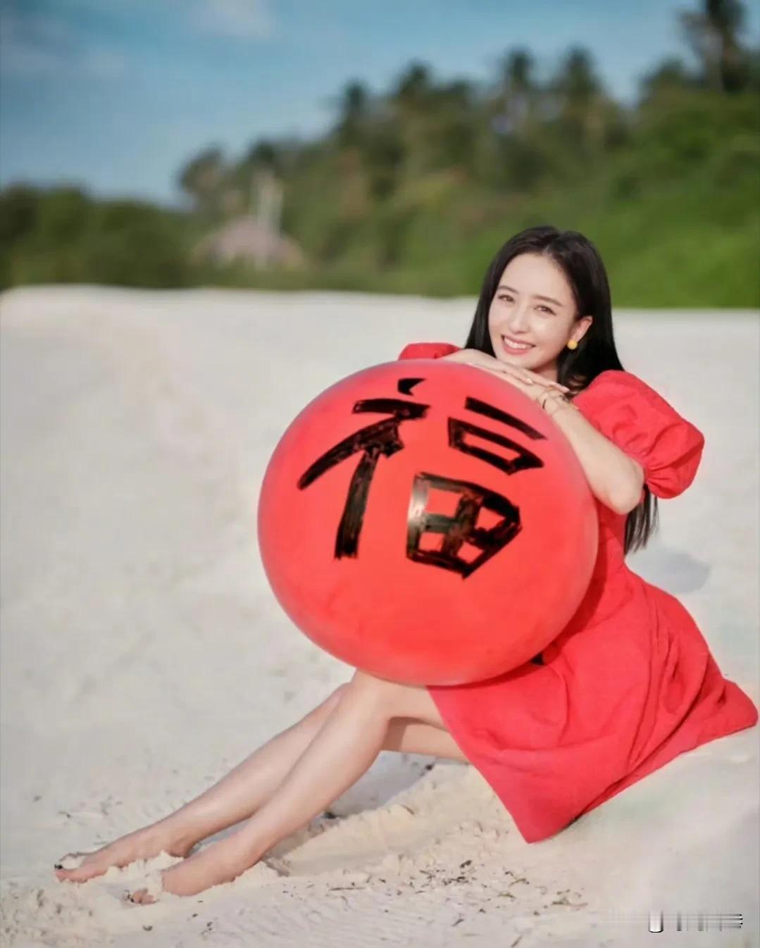 灿烂的阳光下，金色的沙滩上，佟丽娅丫丫穿着一身中国红的裙装，怀里抱着大红色的写着