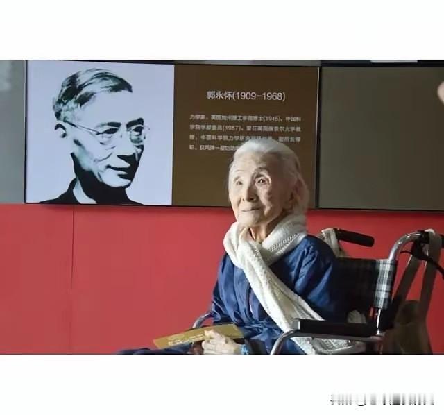 98岁的李佩先生坐在轮椅上，静静地凝望着展板，身后屏幕上印着丈夫郭永怀的黑白肖像