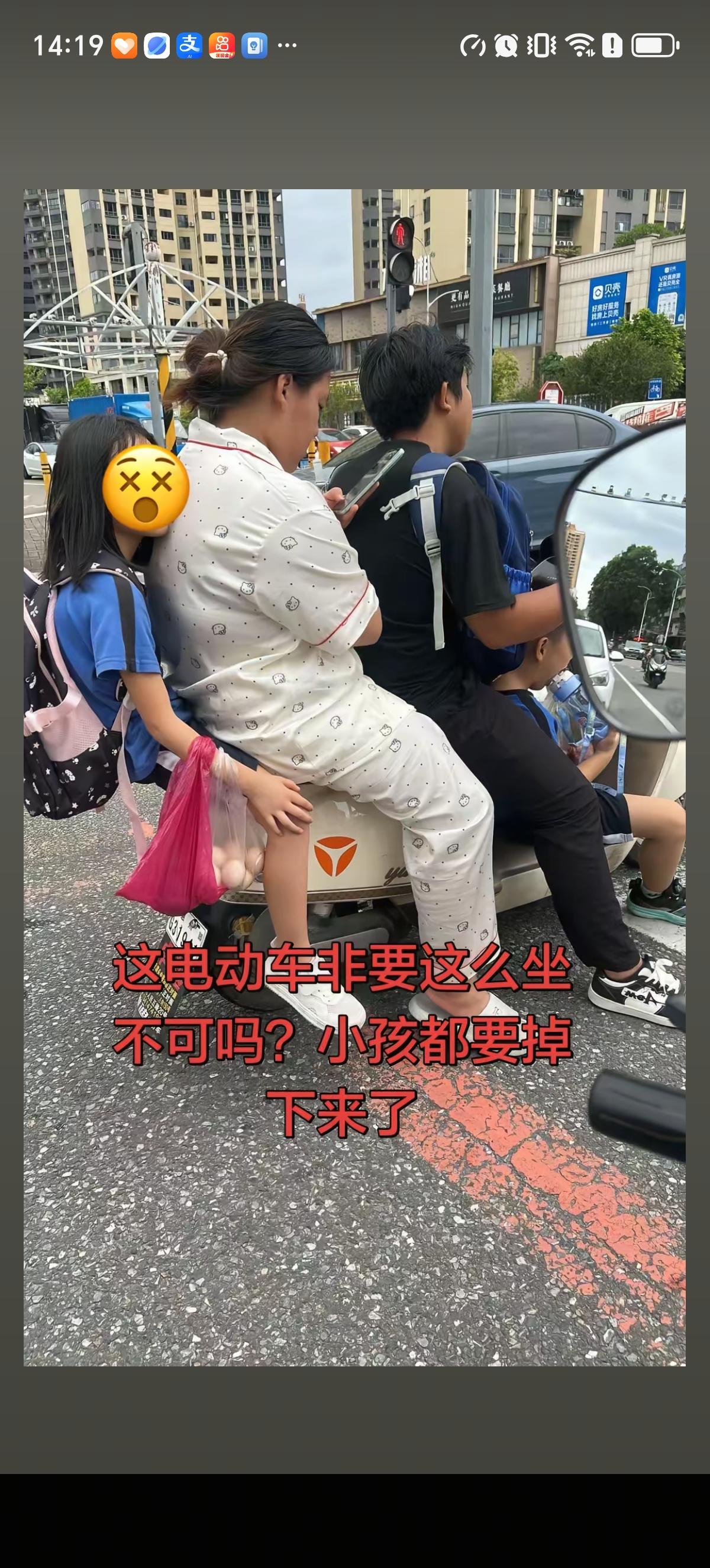 父母接儿子和女儿放学，一家四口骑着一辆电动车，儿子坐在前面的脚踏板上喝水，爸爸负