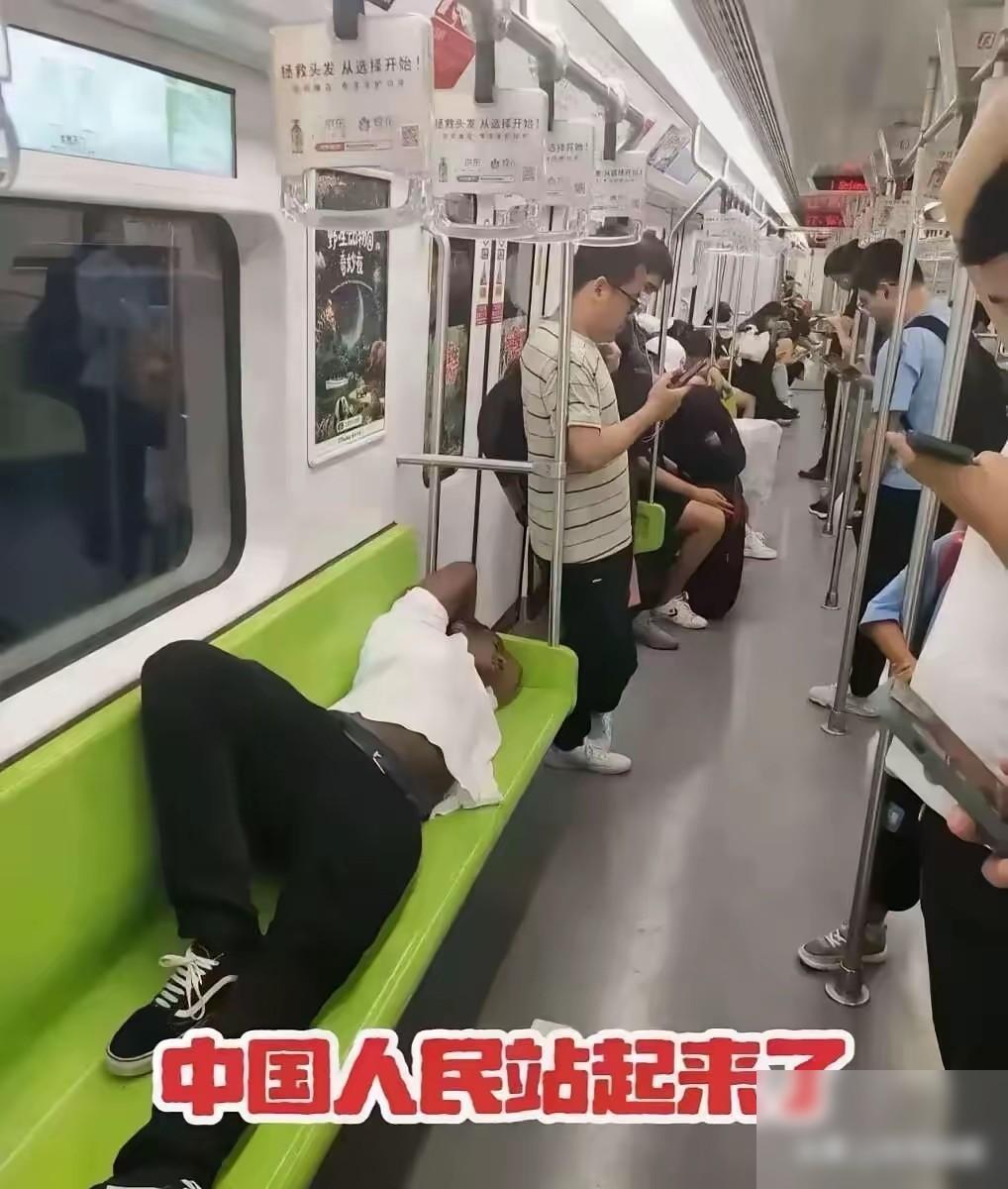 地铁车厢里，长椅被一人横躺占满，其他人齐刷刷站成一片。这个画面扎眼，不只是因为有