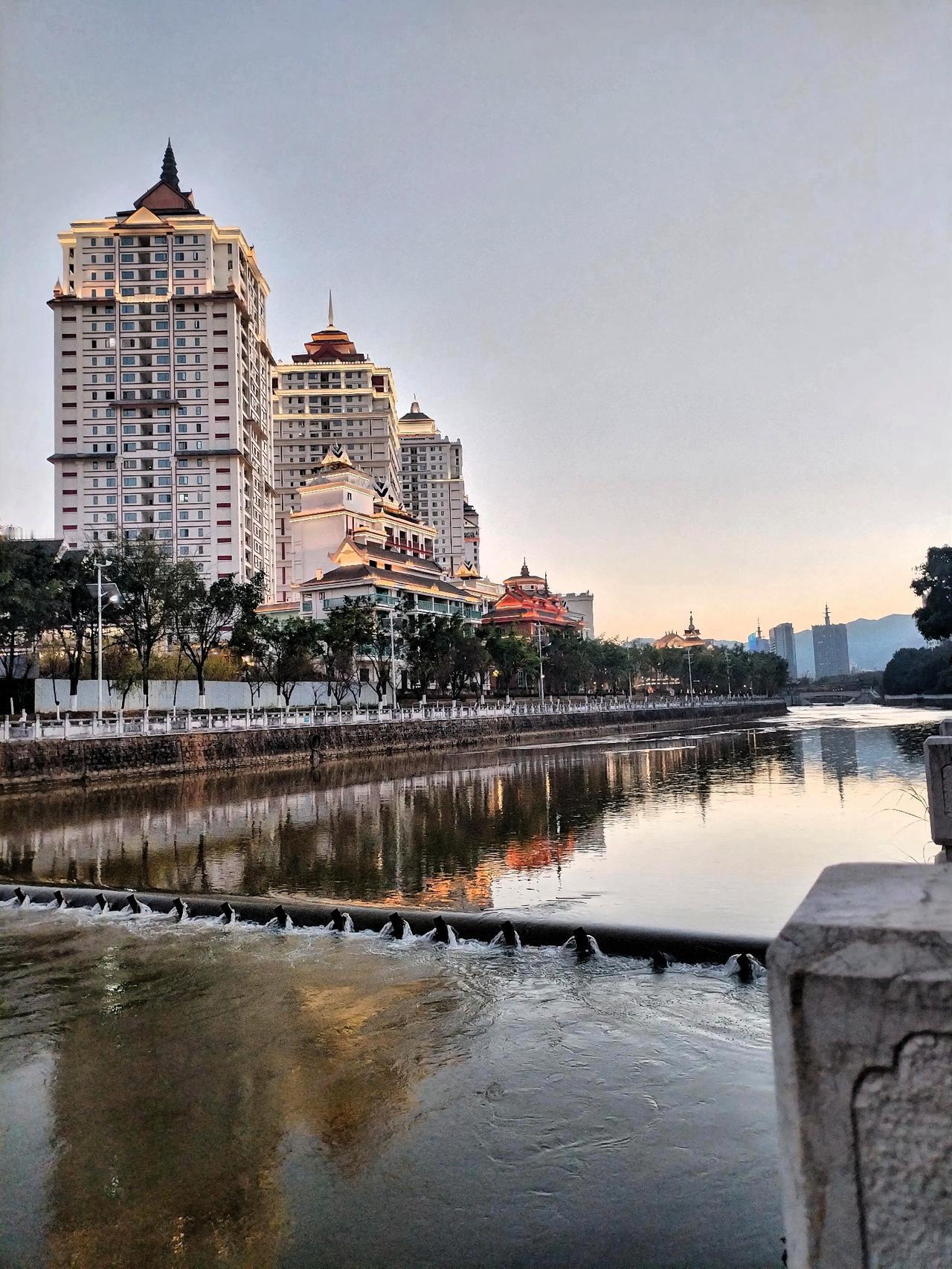 城市河畔的宁静黄昏，倒映着现代与传统的交融。河面上，夕阳的余晖洒下，波光粼粼的金