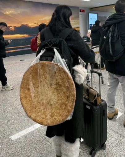 一女子在机场等着过安检，万万没想到女子的背上竟然背了一个硕大无比的馕，远看这馕占