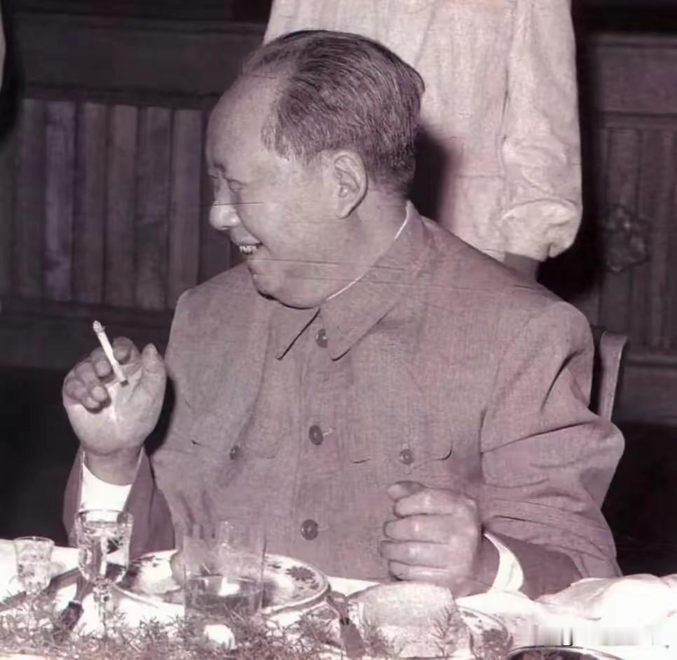 这张黑白老照片里，毛主席身着中山装端坐餐桌前，手中轻捏香烟，侧脸开怀大笑，神情松