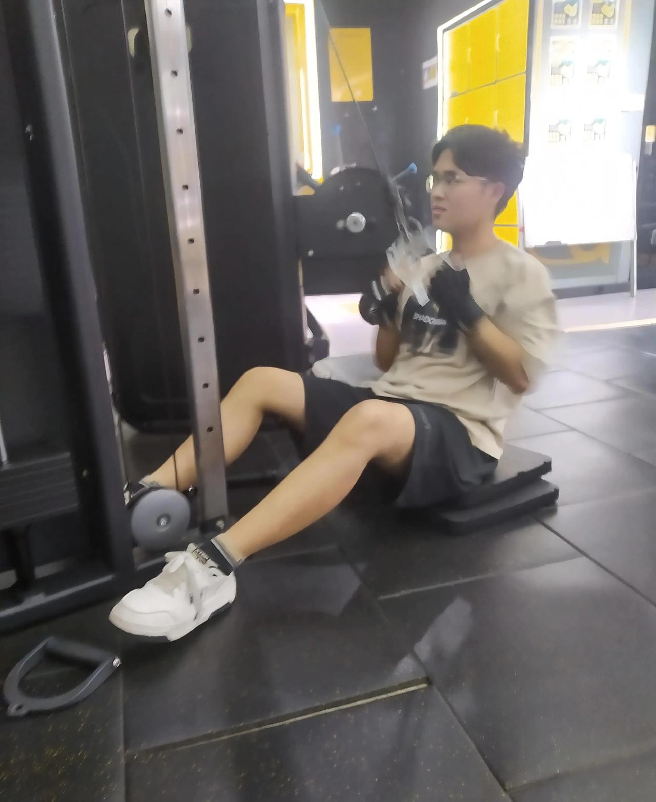 健身房里这哥们儿的状态太真实了——戴着手套绷着劲儿，动作里带着点“新手式认真”。