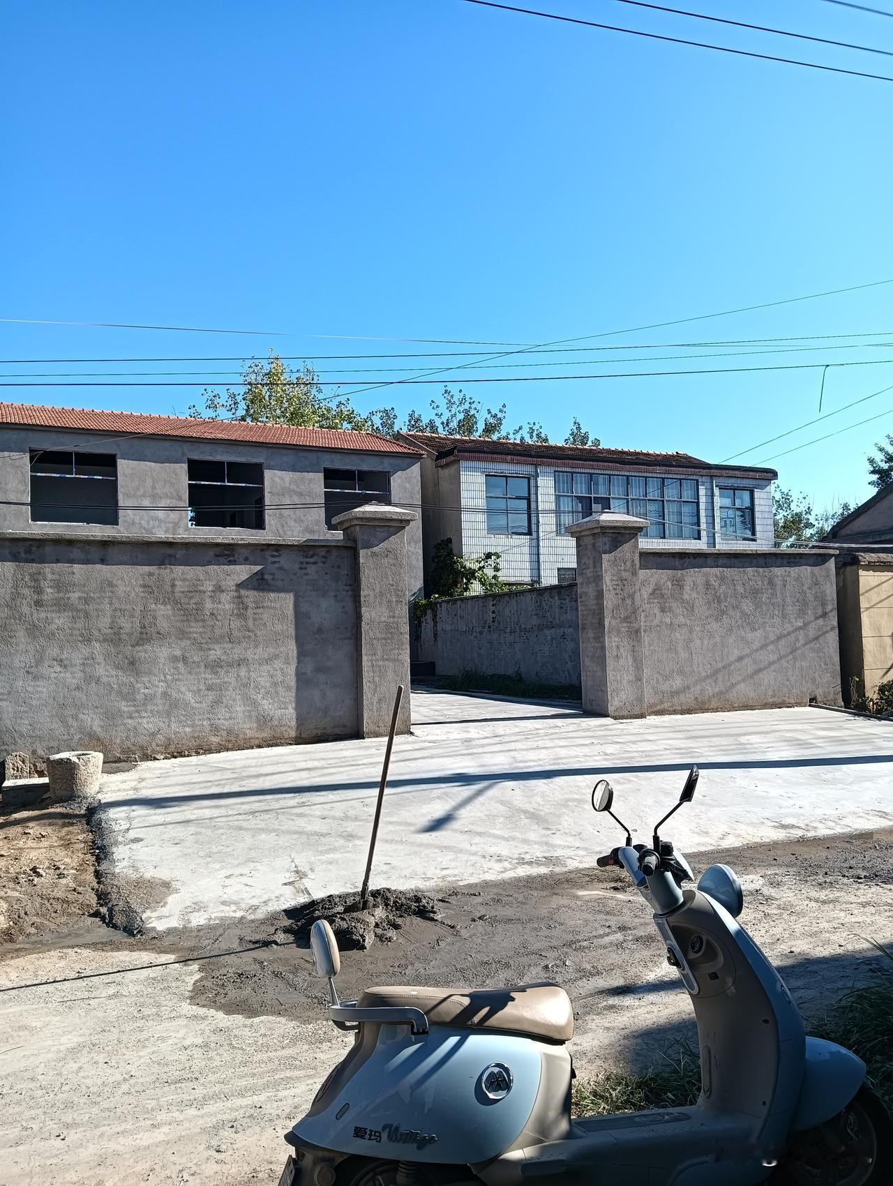 院子里停着一辆摩托车，工人们正在院子里打地坪。天气晴朗。