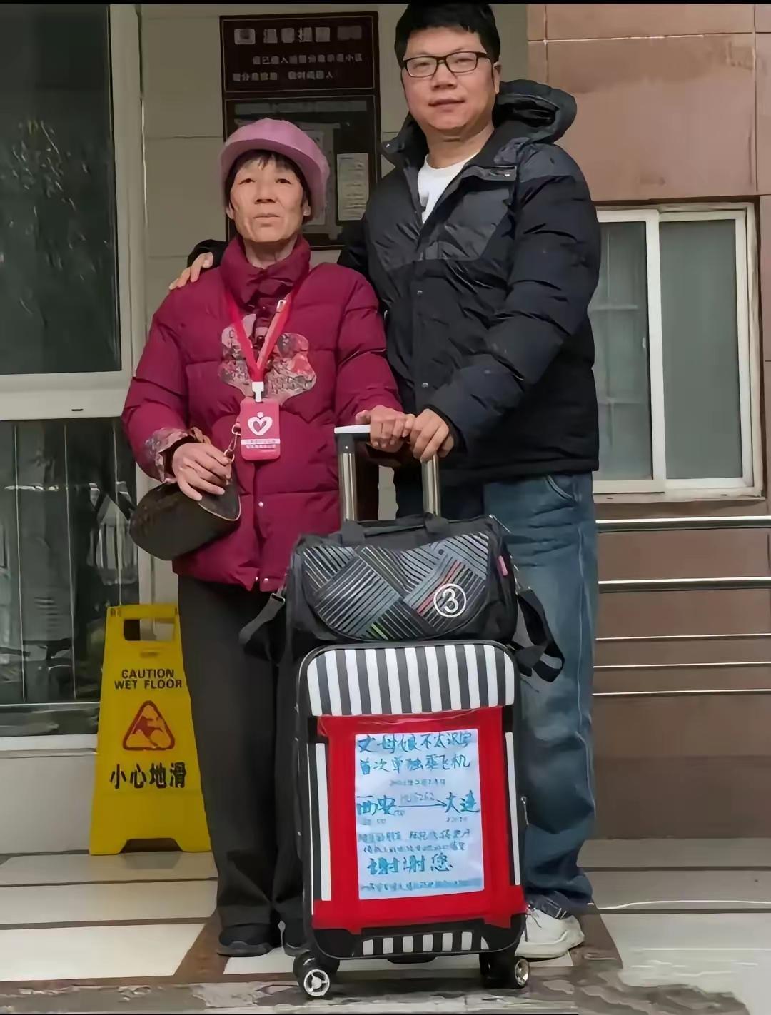 机场里，小伙子给丈母娘送行，老人的行李箱上贴着一张纯手工写的大海报，上面写着:“