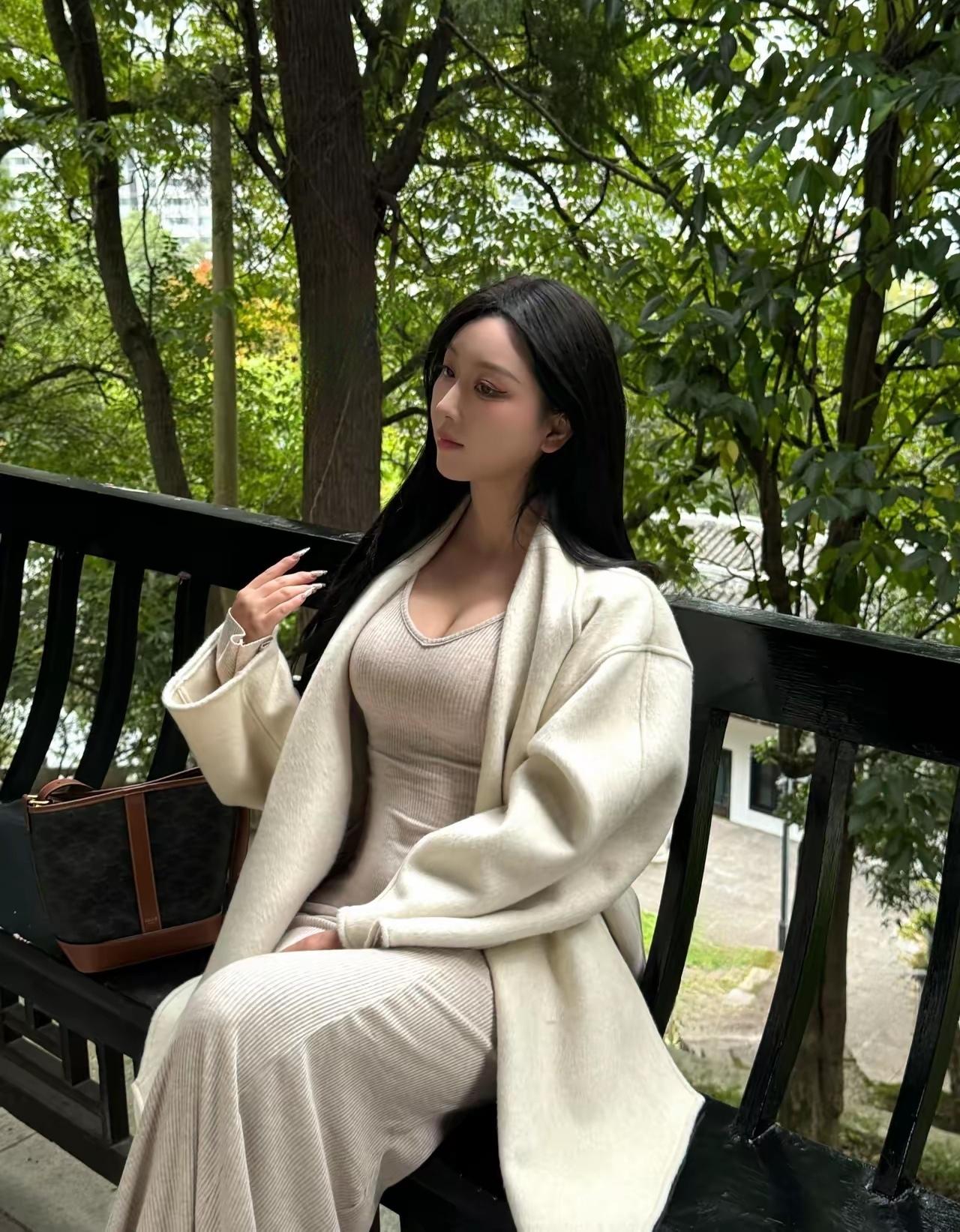一个穿白色大衣的女士坐在长椅上。
