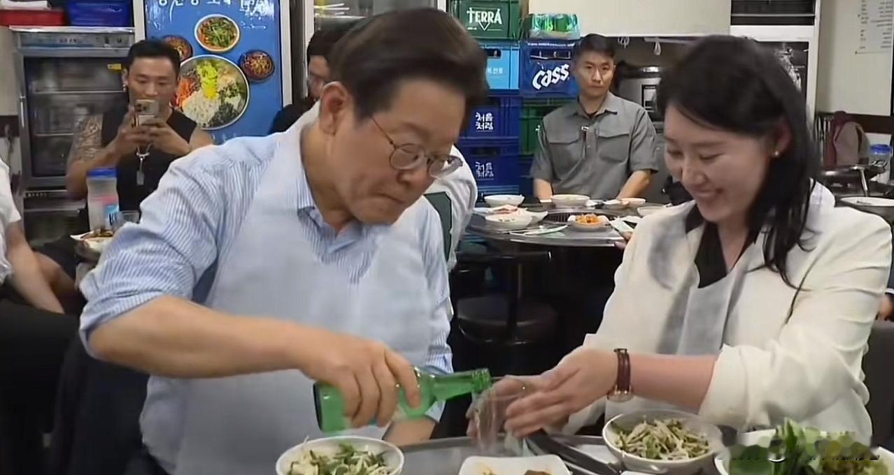 李在明挽起衣袖，自己拿起酒瓶和酒杯给随行人员先倒酒，先倒一点烧酒，然后再倒满啤酒