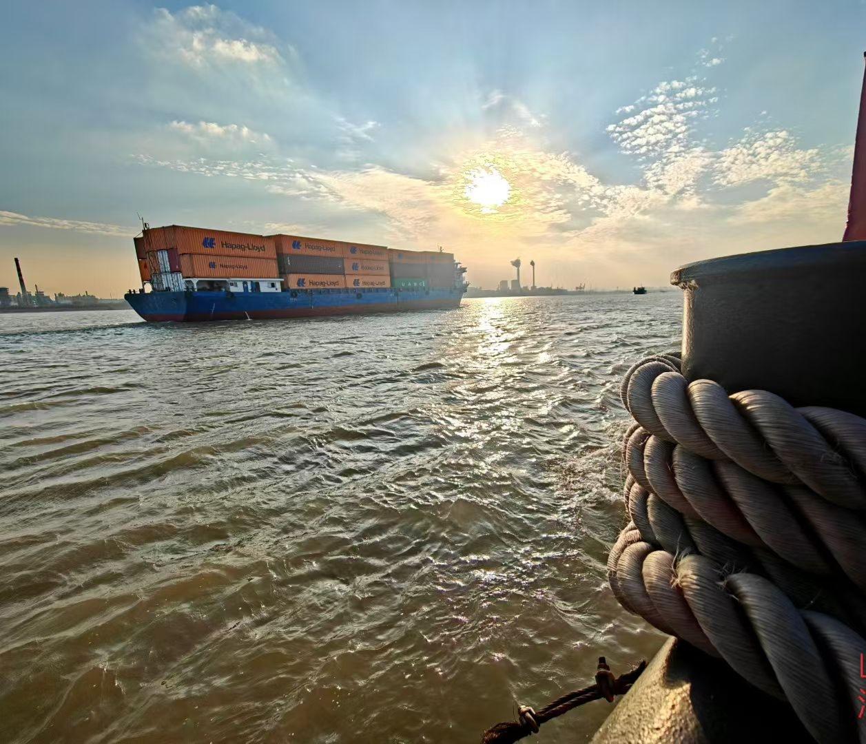 发张你手机里最美的夕阳照。落日把波光揉成碎金，货轮载着橙箱在风里赶路。船舷的绳结