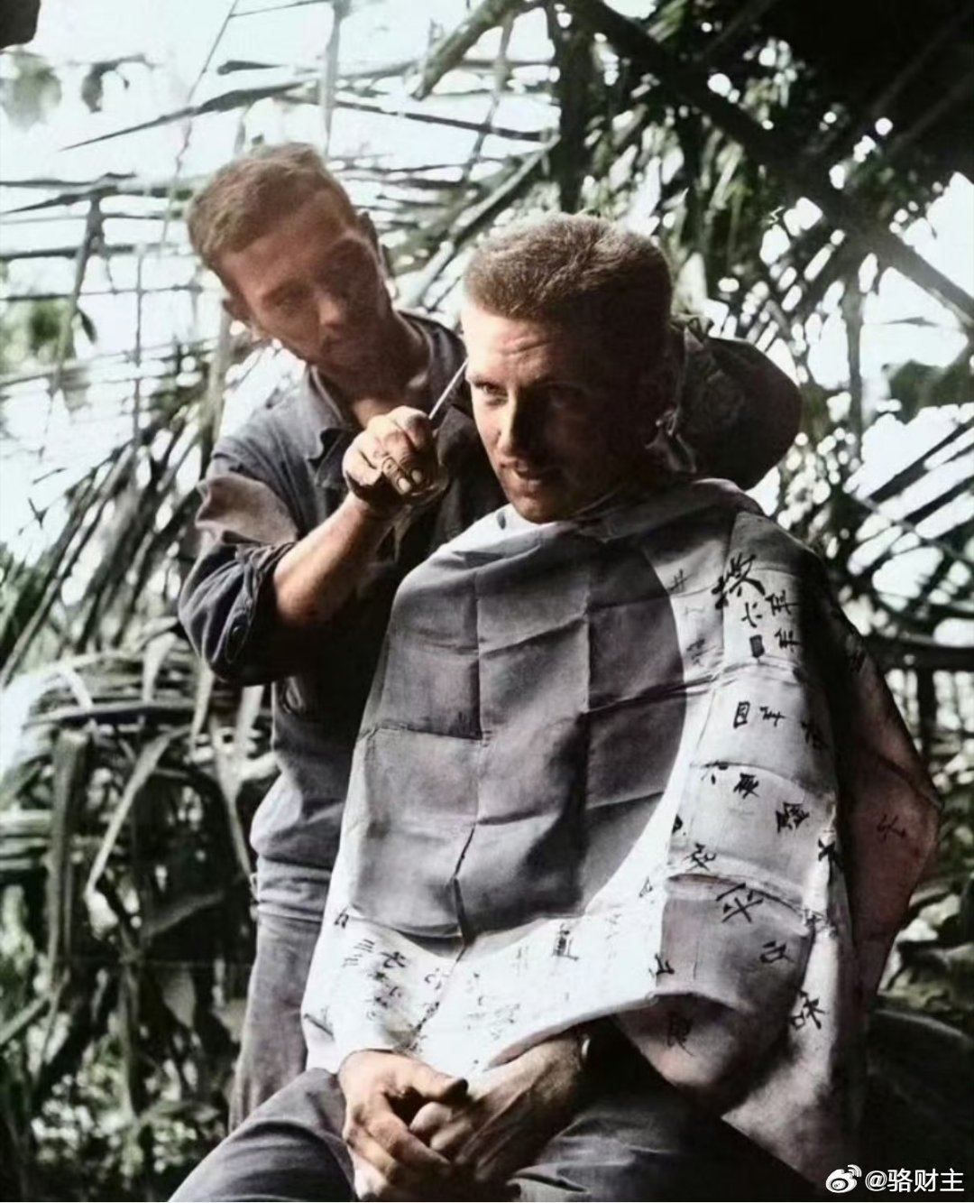 二战期间，一名美国大兵正在用缴获的日本国旗，当成理发的围布，给战友理发。这面太阳