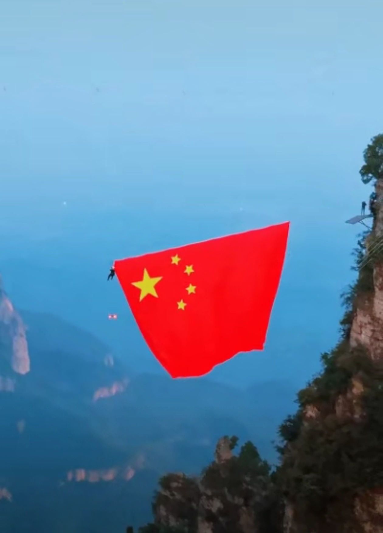 河南云台山，一名网友爬到半山腰，正累得不行，忽见工作人员在悬崖间悬挂巨幅五星红旗