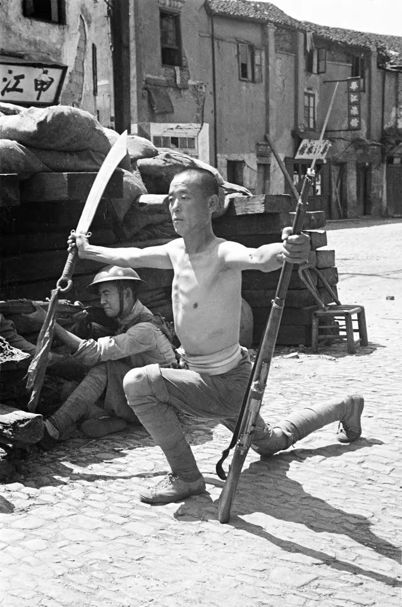 1937年，日军进攻上海。在街道上，一名中国士兵赤膊上阵，向战壕对面的...