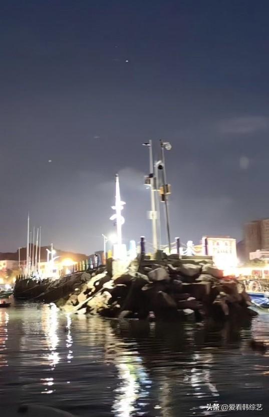 夏日生活打卡季夜色浸染港湾，岸边灯火垂落河面碎成粼粼银波。礁石静立水边，帆船桅杆