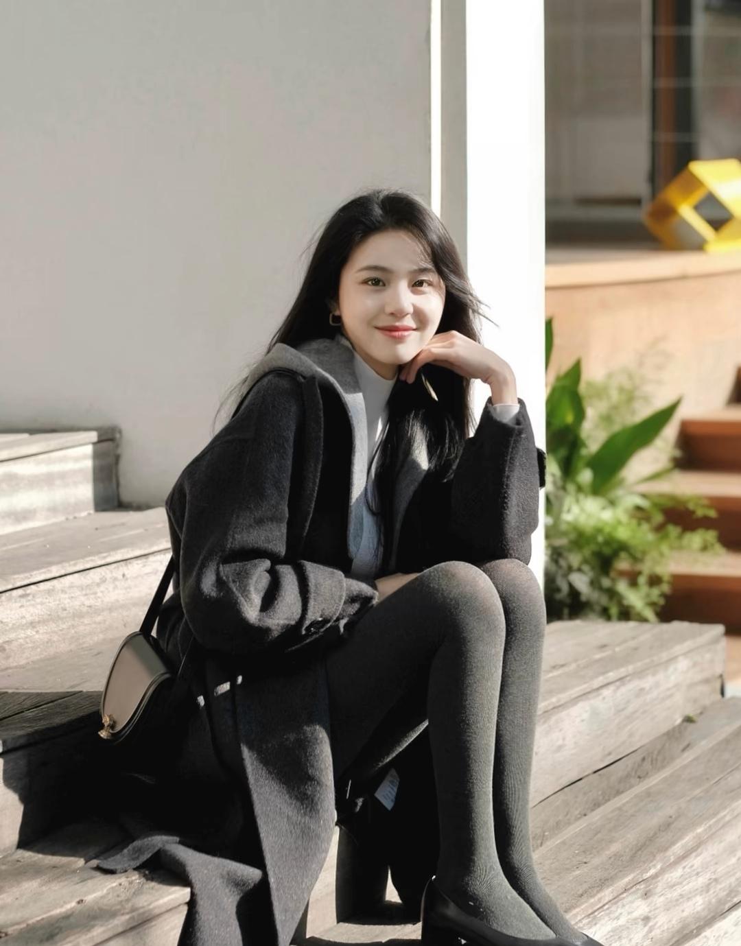 阳光下的温暖时光，黑衣少女静坐台阶，微笑如春日暖阳。