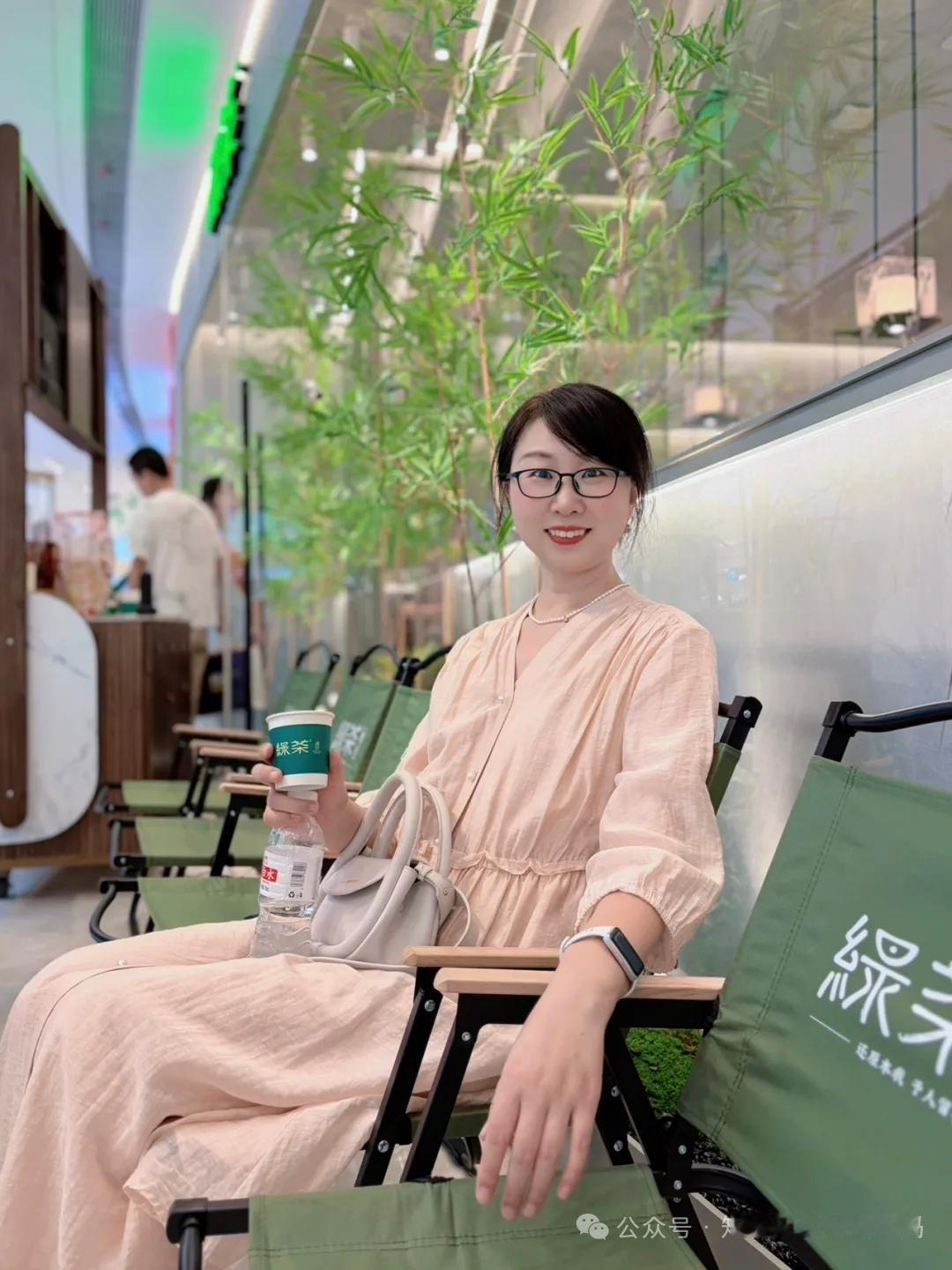 女孩坐在椅子上喝奶茶，很惬意。