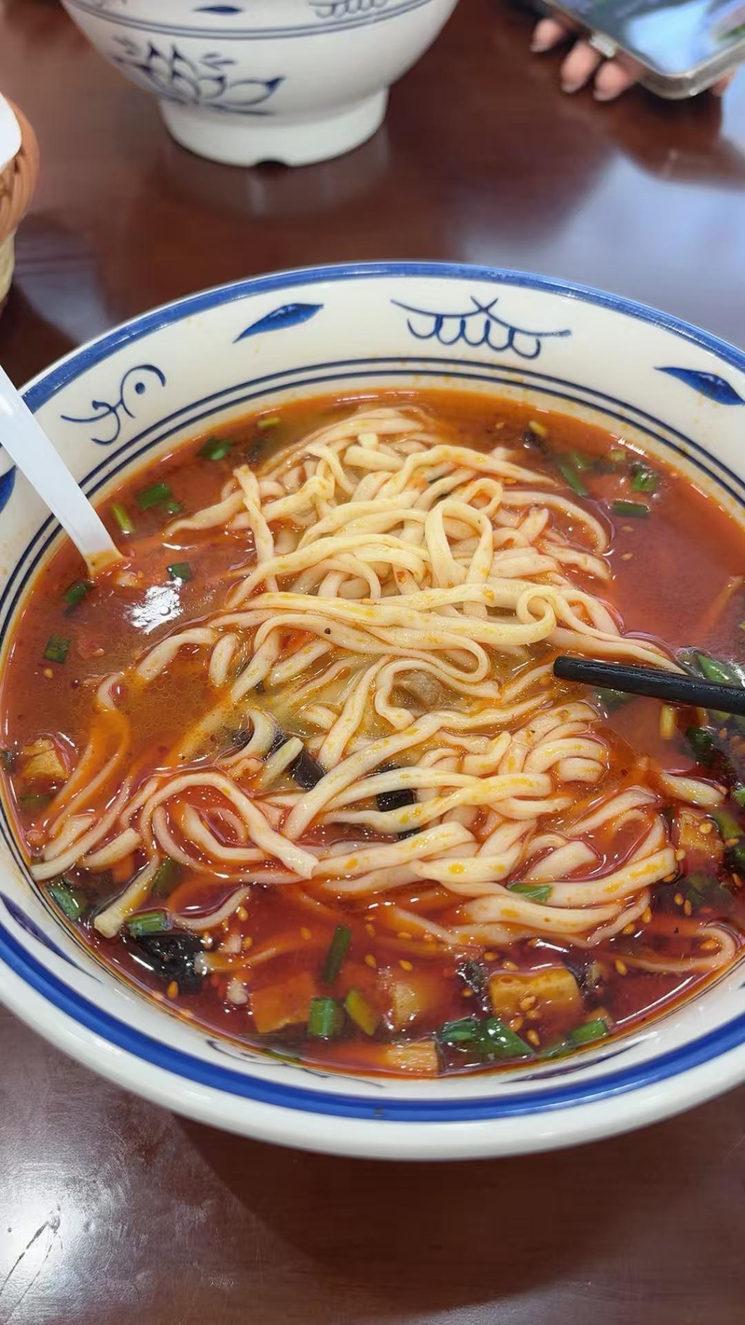 这碗面看着就带劲！红油汤底红亮诱人，面条根根裹满了汤汁，配上葱花和配菜，光看着口