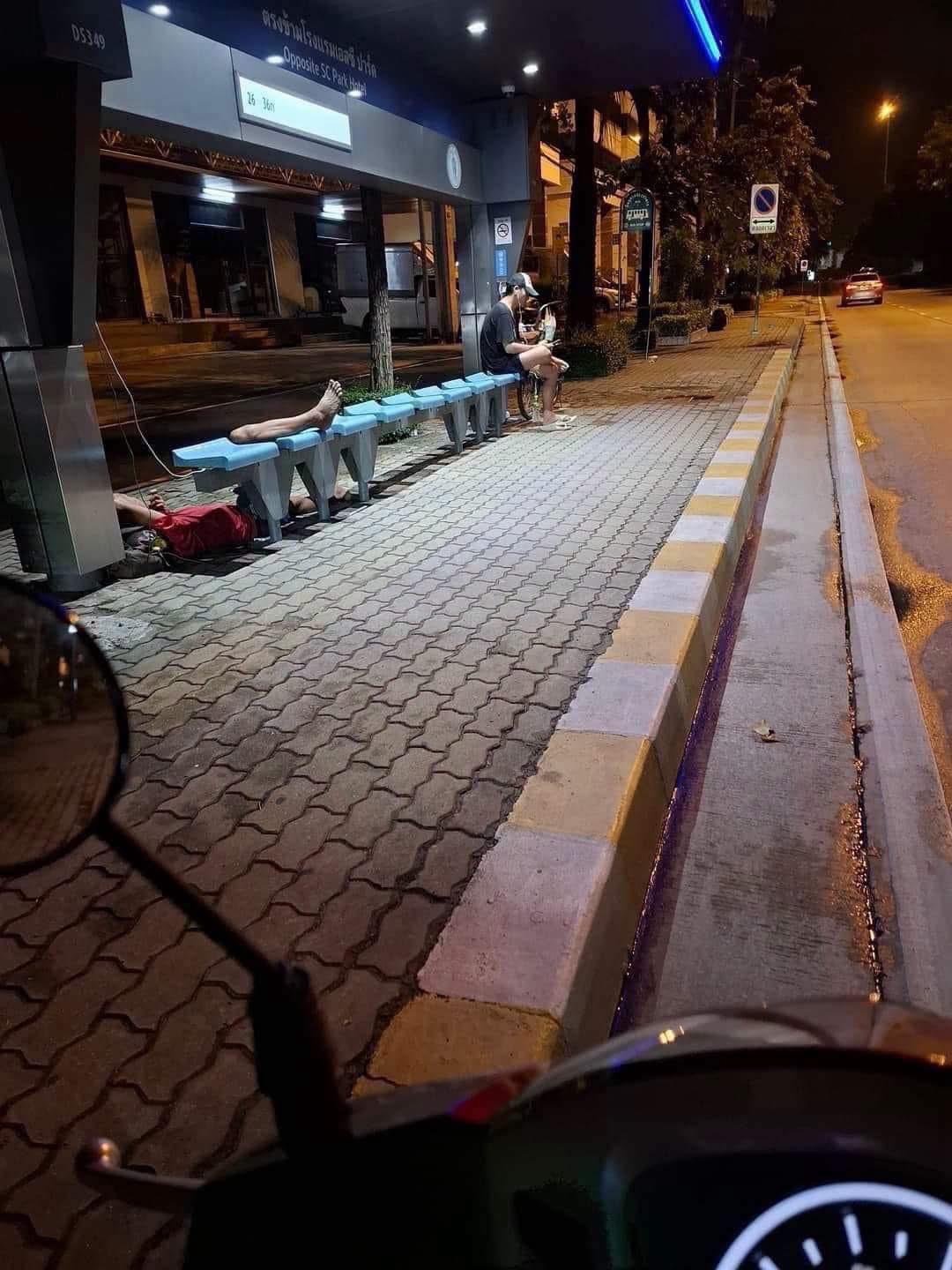 深夜的泰国街边车站。
长椅被分成了两半。
一个人蜷缩躺在长椅下方酣睡，双腿搭在椅