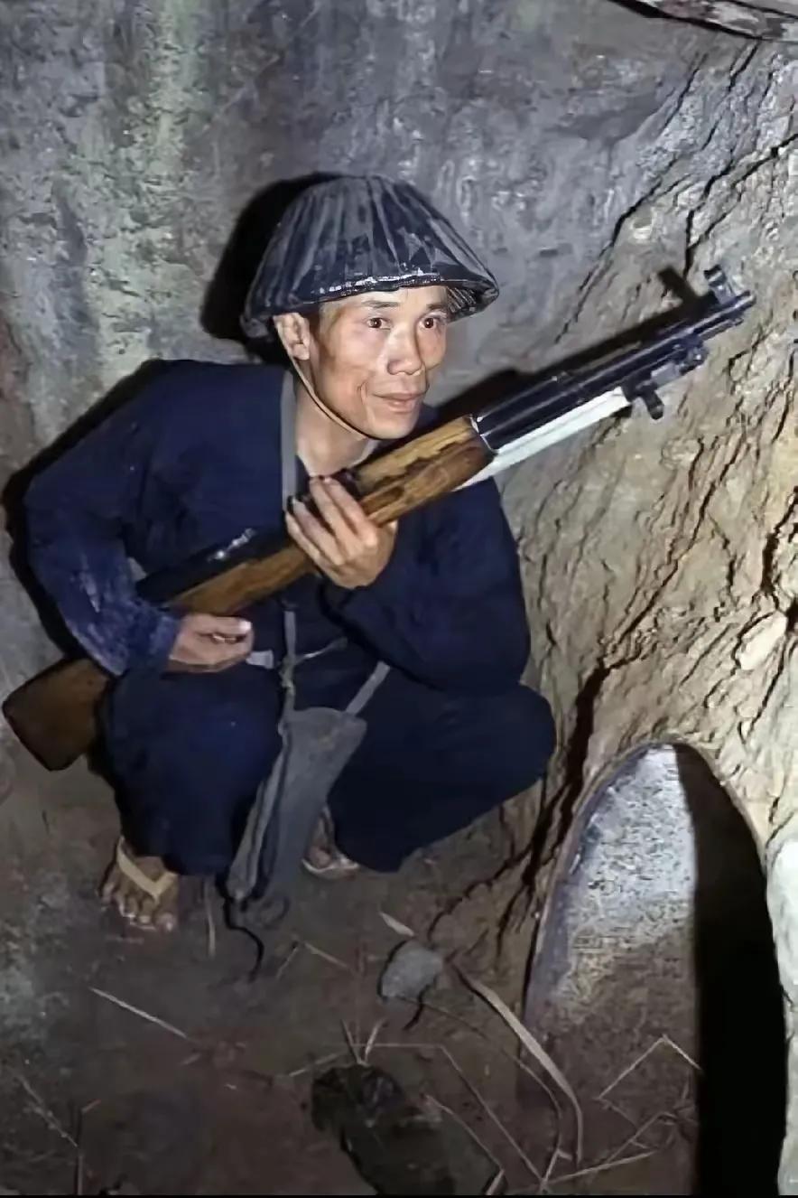 这是当年越南的一名民兵，他手握着中国支援的步枪，蹲在猫耳洞里，前面是一个大铁桶做
