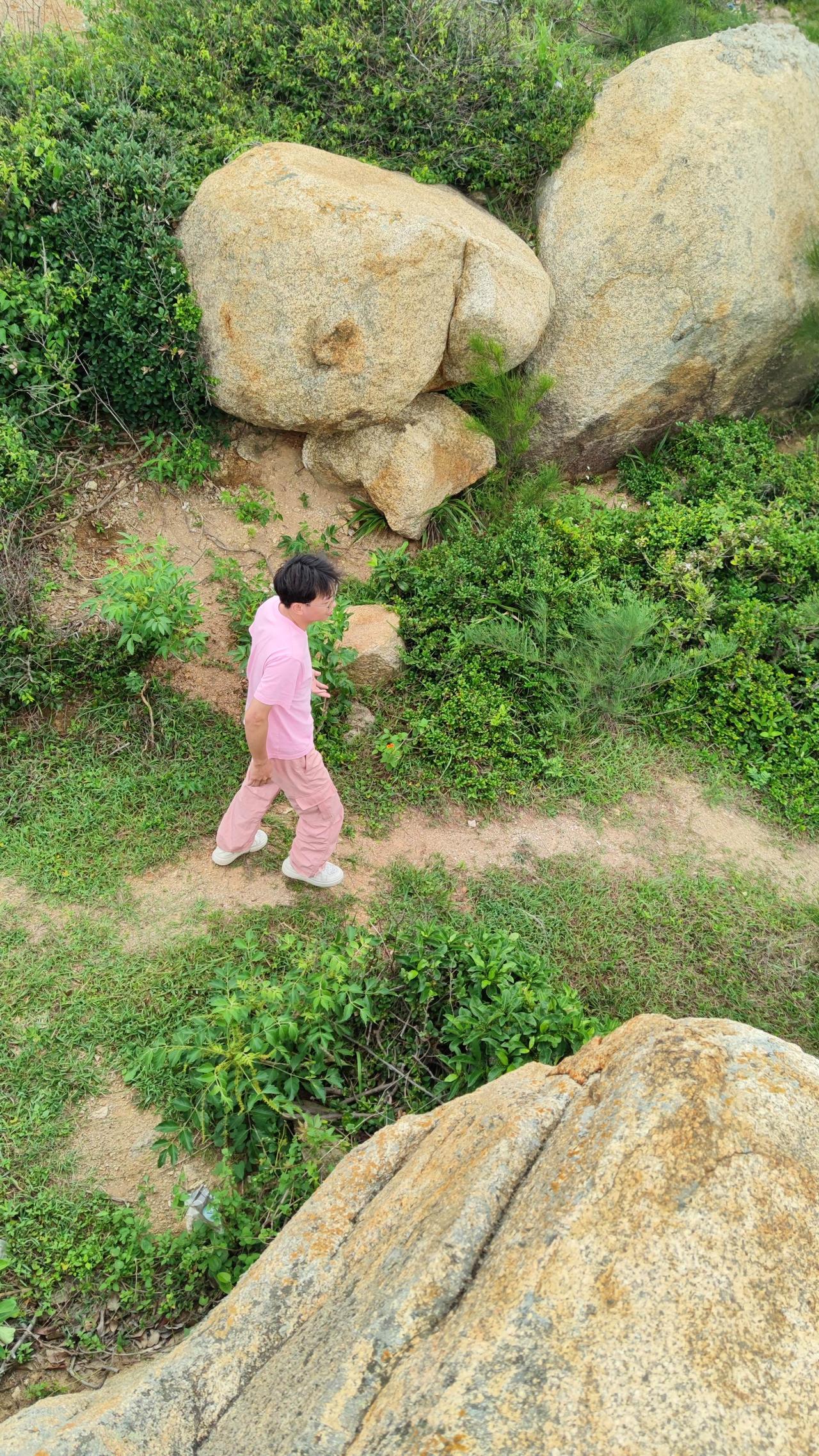 穿行山野乱石间，脚下土路蜿蜒，四周草木簇拥着大块岩石。一身浅粉穿搭融在满眼绿意里