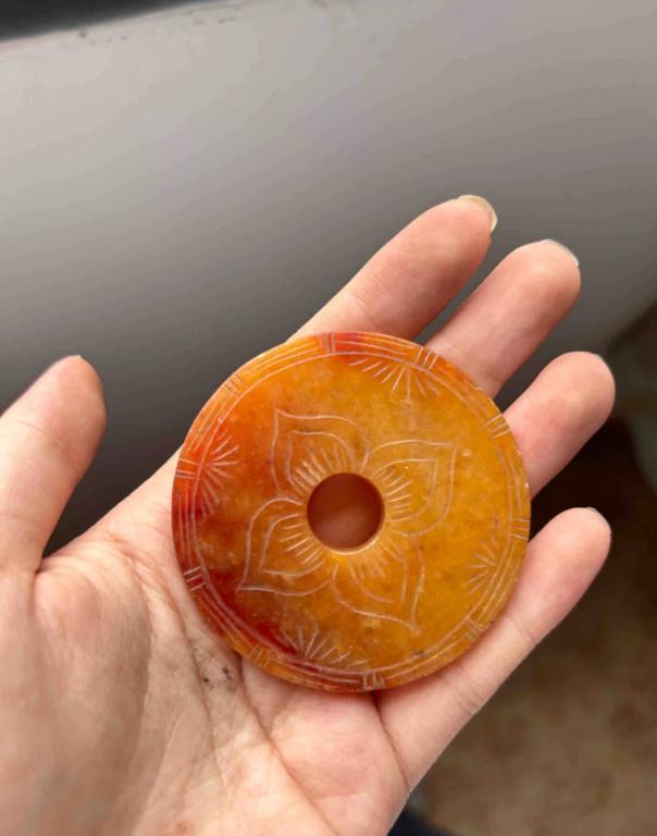 在古玩城一个摊上看到一个玉璧，圆的，中间一个孔，橙红色的，半透明，正面刻了一朵花